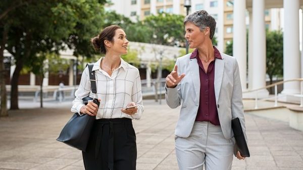 Two business women in conversation walking on city street. Corporate colleagues discussing new project while going to work. Two mature formal women discussing business outdoor.