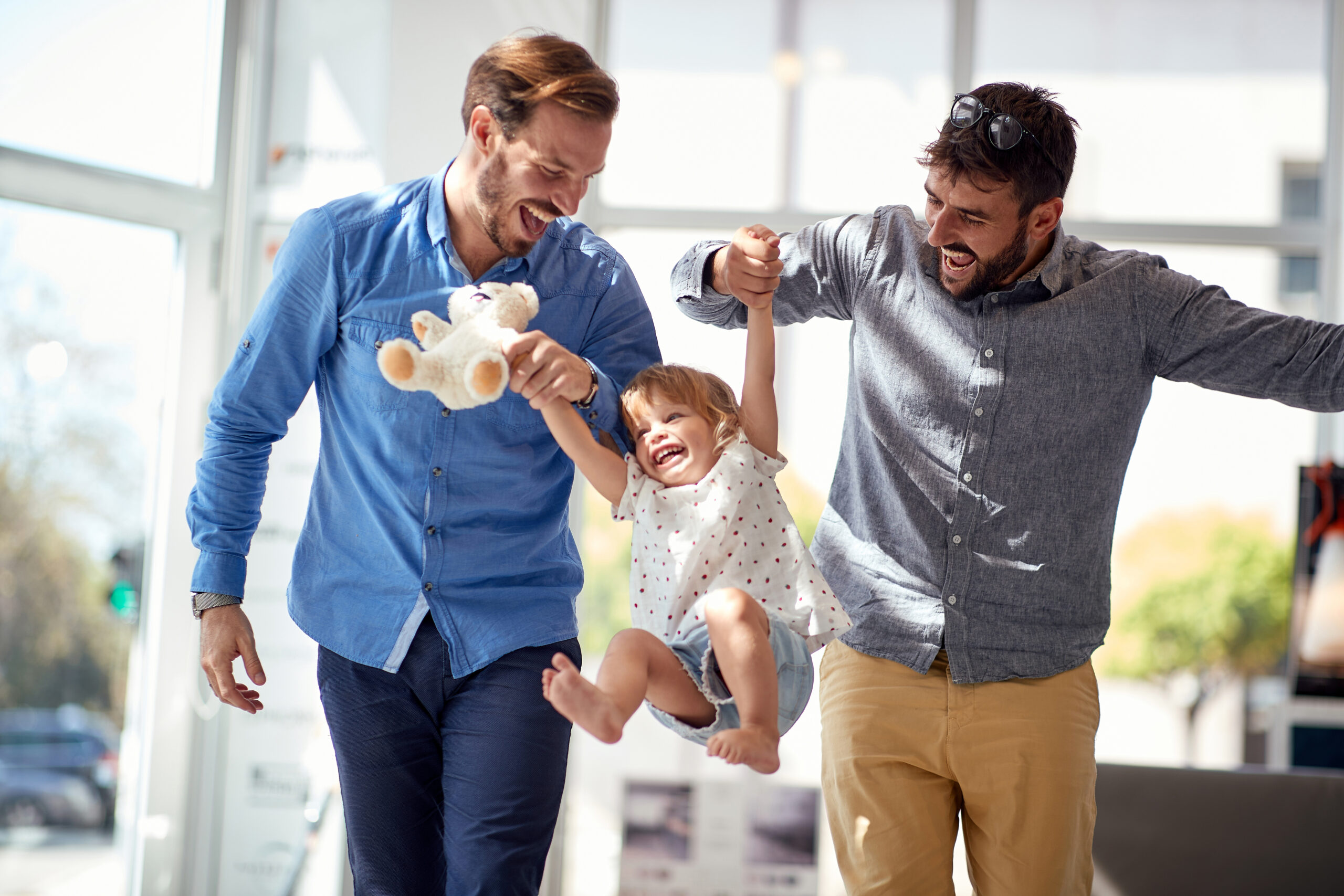 Two fathers swing their happy daughter in the air.