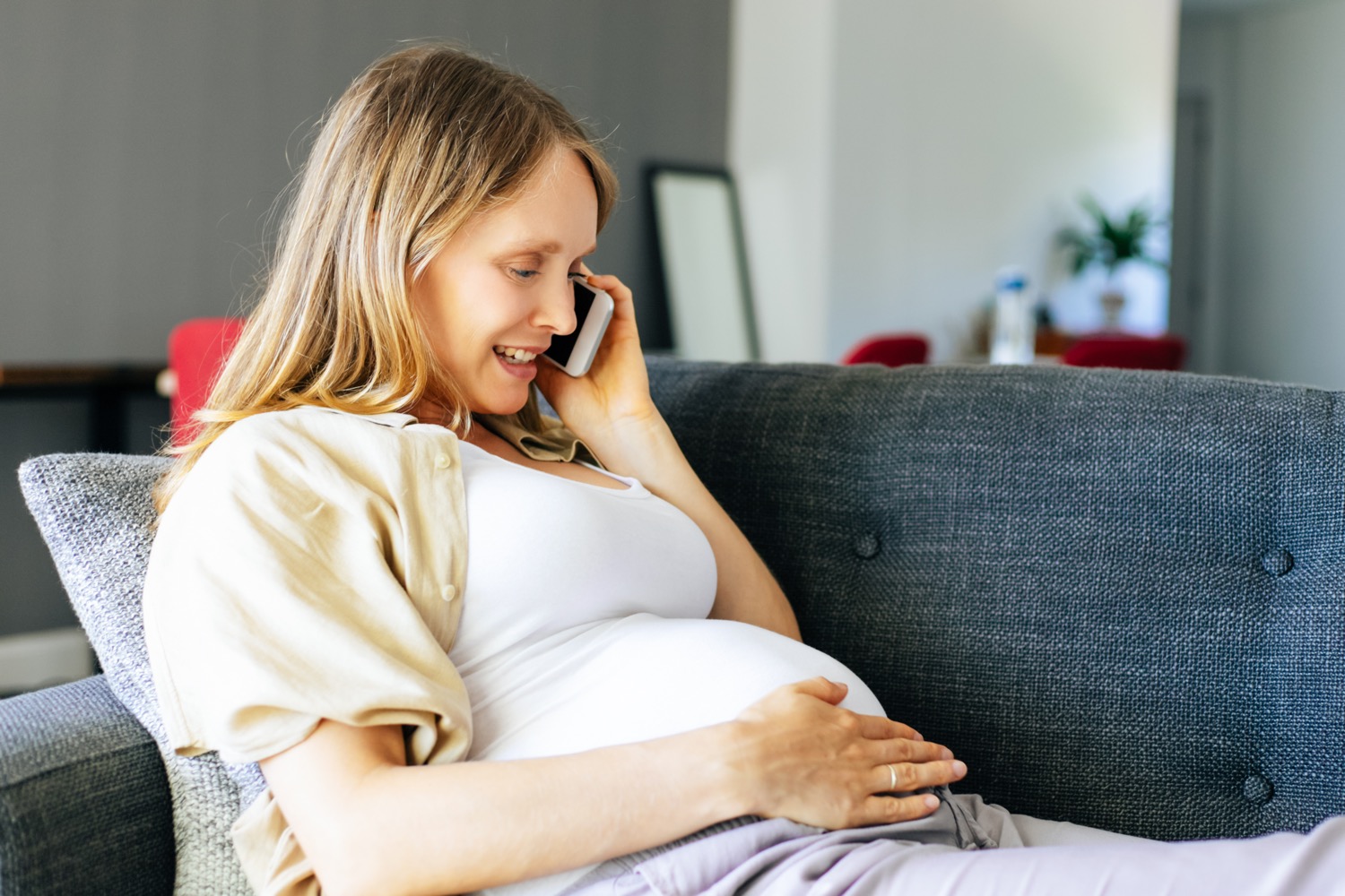 a pregnant woman sits on her couch talking on the phone to her surrogacy attorney