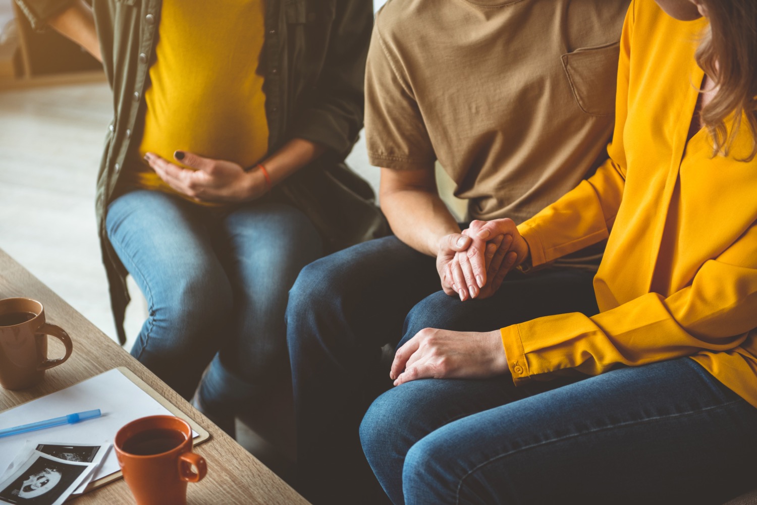 after gaining an understanding of surrogacy costs, a couple sits on a couch with their surrogate looking at ultrasound images