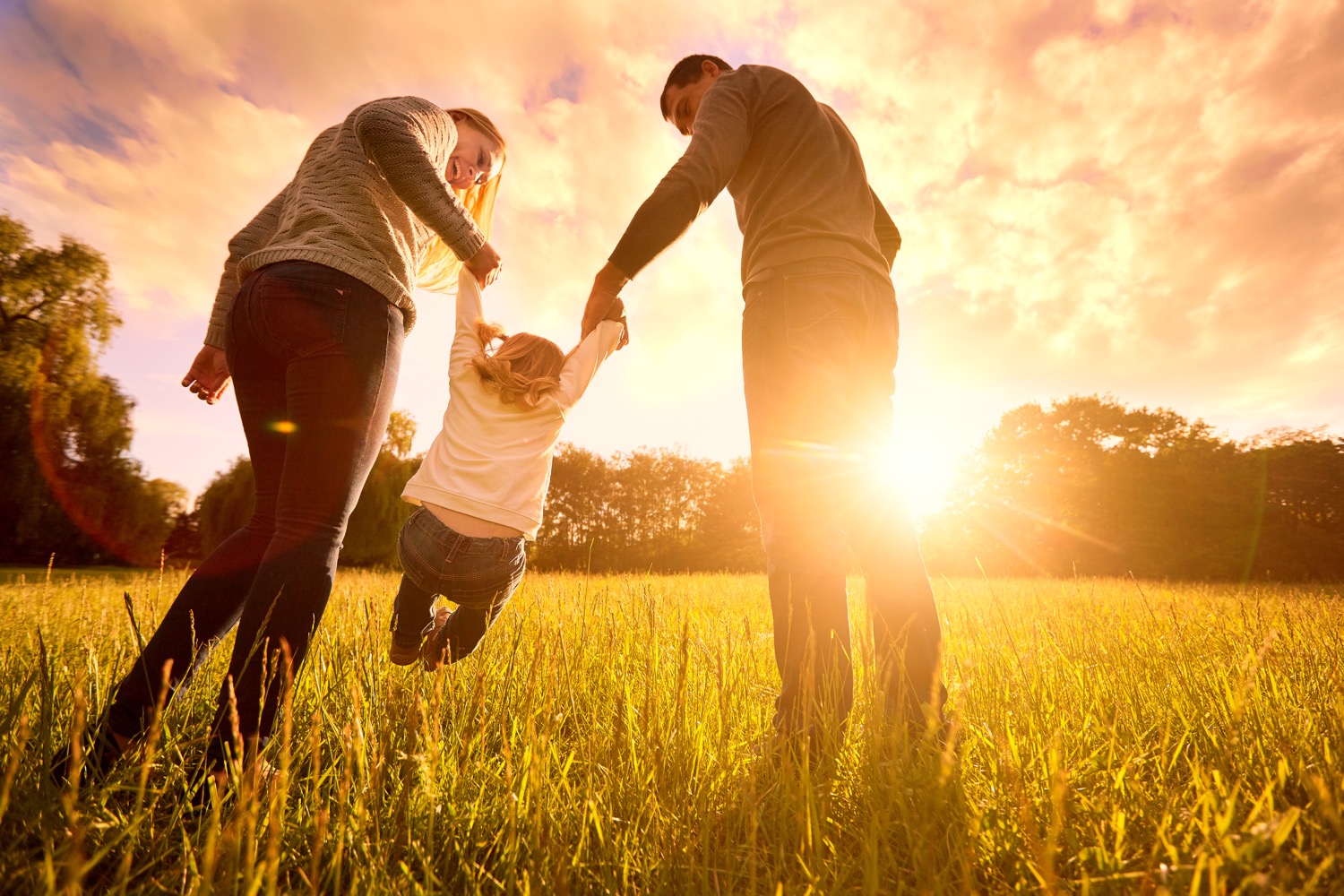 A couple swinging their adopted child through a field at sunset.